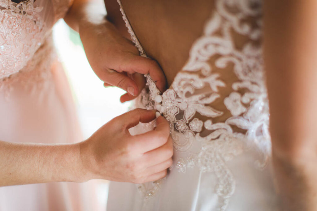 beim Getting Ready wird einer Braut das weisse Kleid von der Trauzeugin am Rücken geschlossen