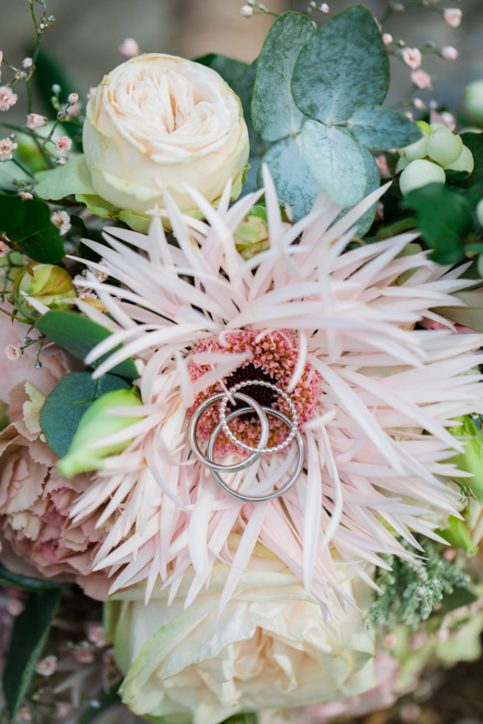 Makroaufnahme von Eheringen auf Brautstrauss mit rosa Blüte