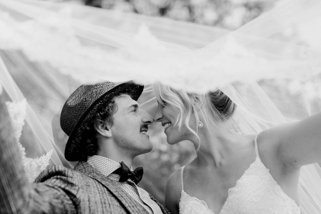 Schwarz-Weiss Hochzeitsfotos von einem Braut, das sich unter dem Schleier der Braut küsst